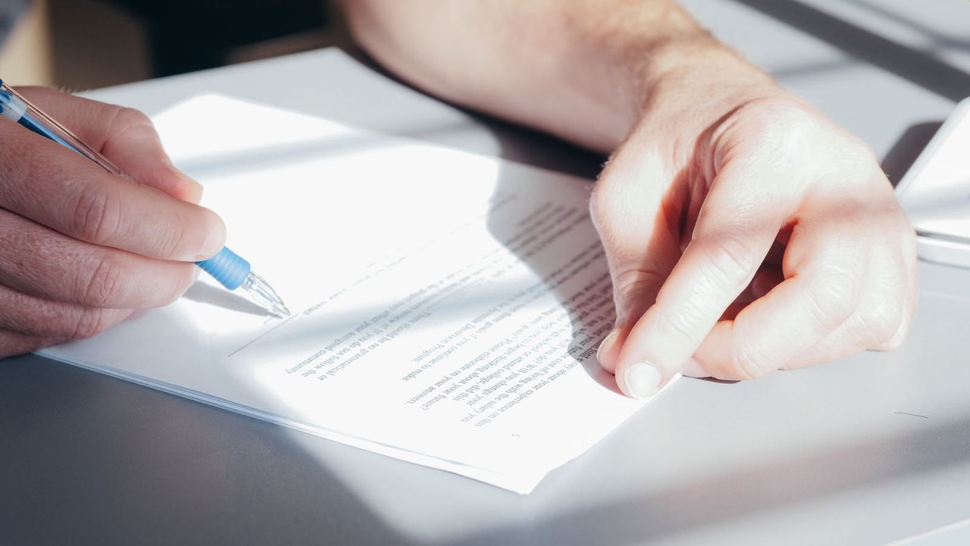 A hand signing an enrollment form with a pen
