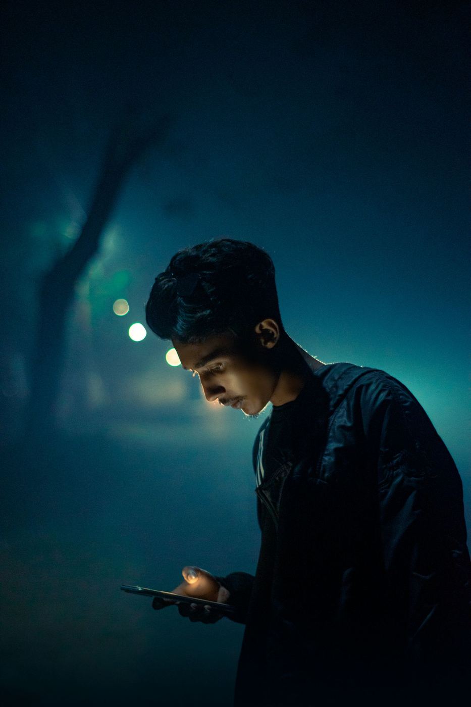 A man alone at night, lit only by his phone screen